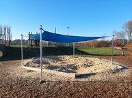 Ein Sandkasten mit Sonnensegel ist zu sehen.